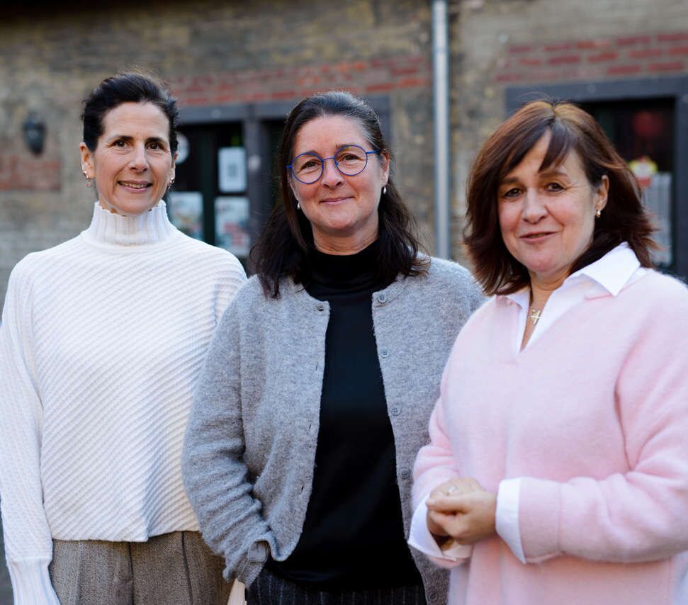 Unsere Koordinatorinnen stehen im Freien vor einem Backsteingebäude und schauen in die Kamera.